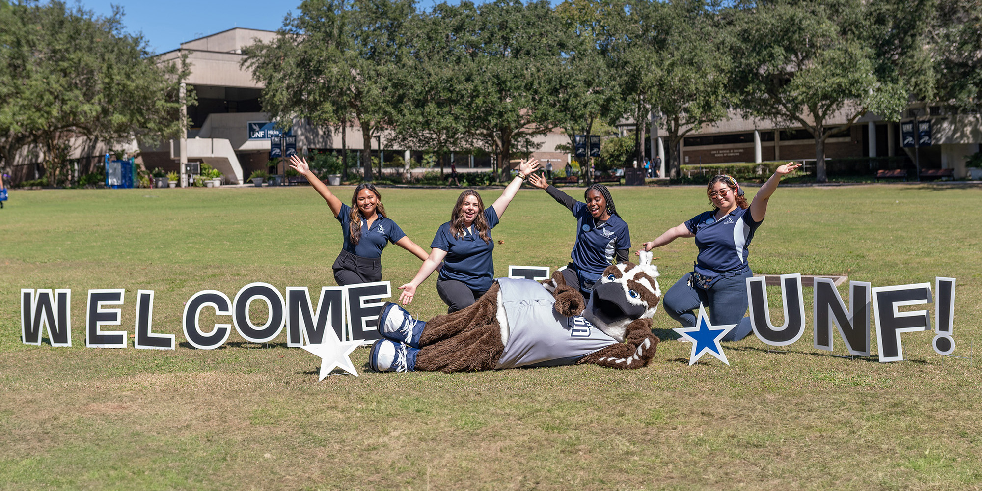 Ozzie and students posing around a welcome to unf sign on campus