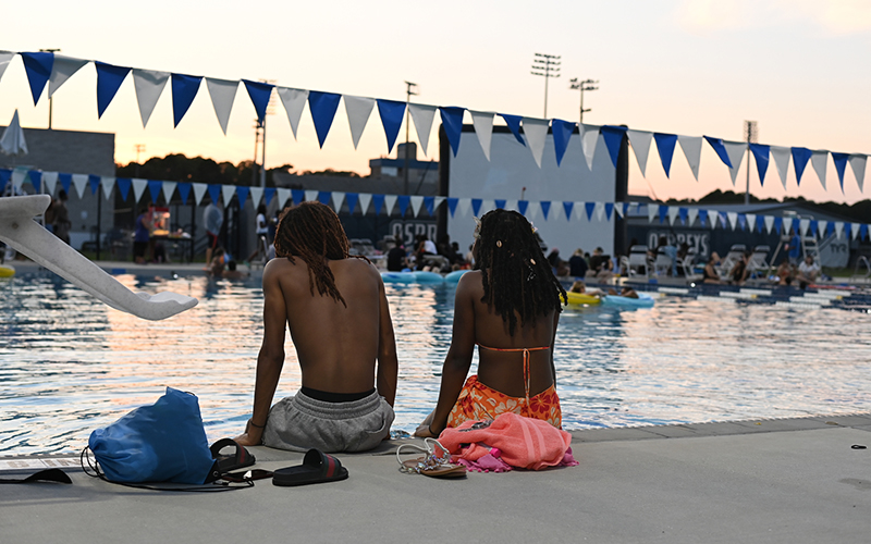two students sitting on the edge of a pool watching a movie
