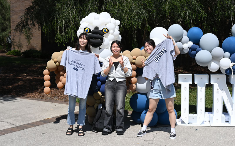 three students with t-shirts smiling with a balloon ozzie in the background