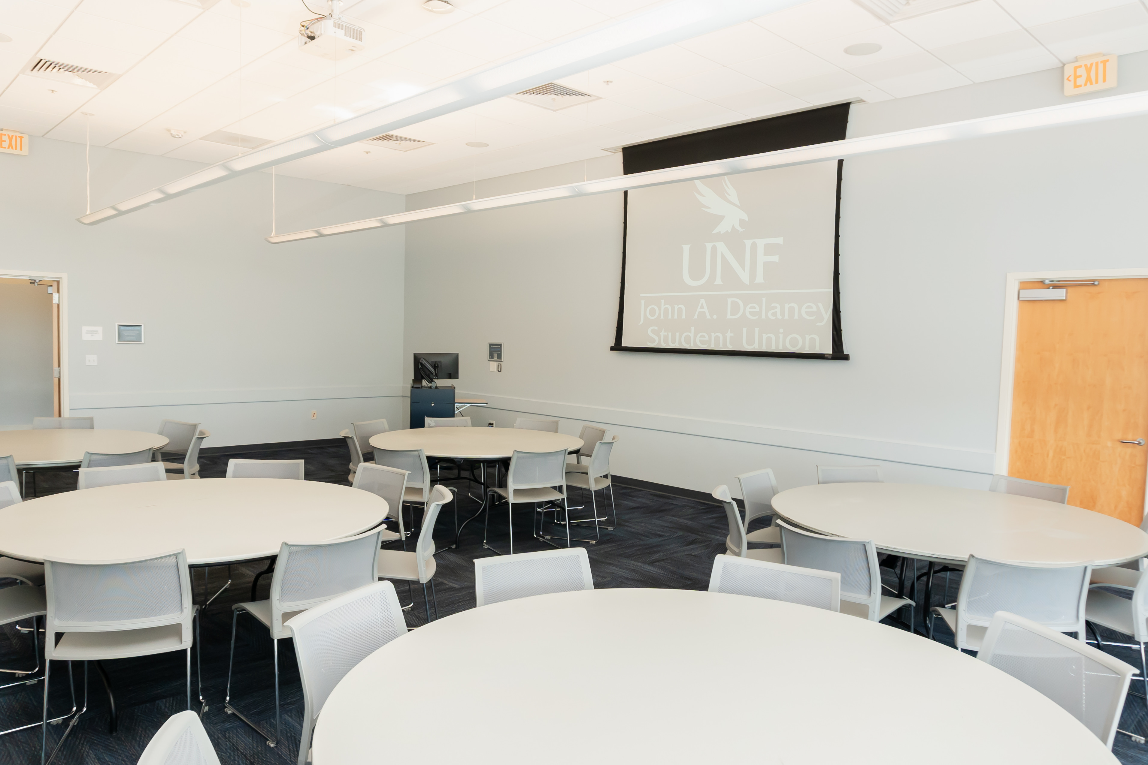 room with round tables, chairs, projector screen, computer