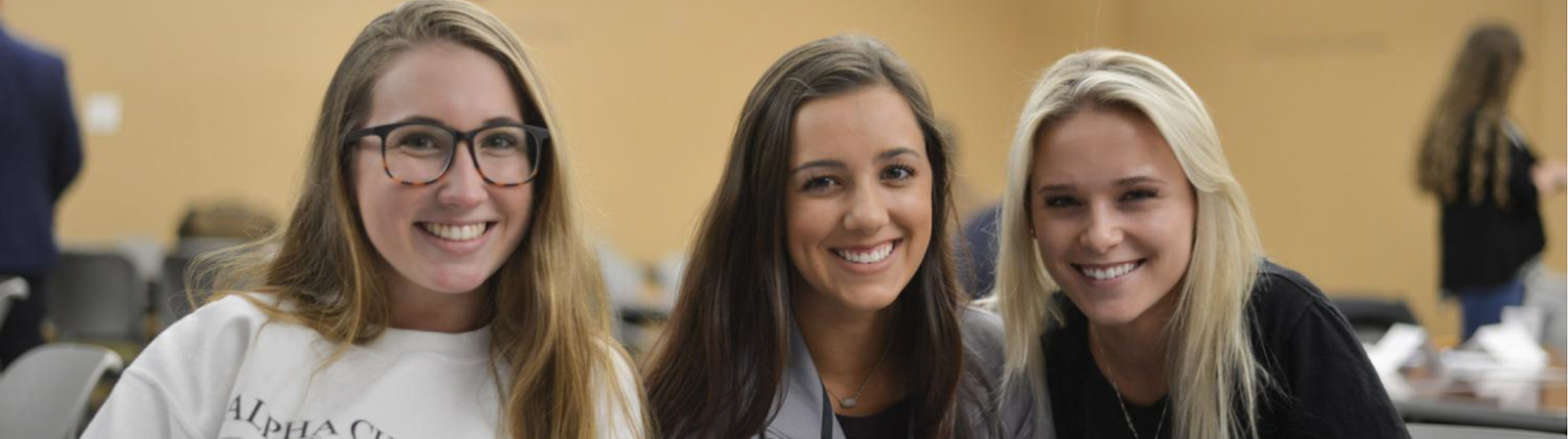 Three female students looking at the camera and smiling during the TLI Mentor Orientation event