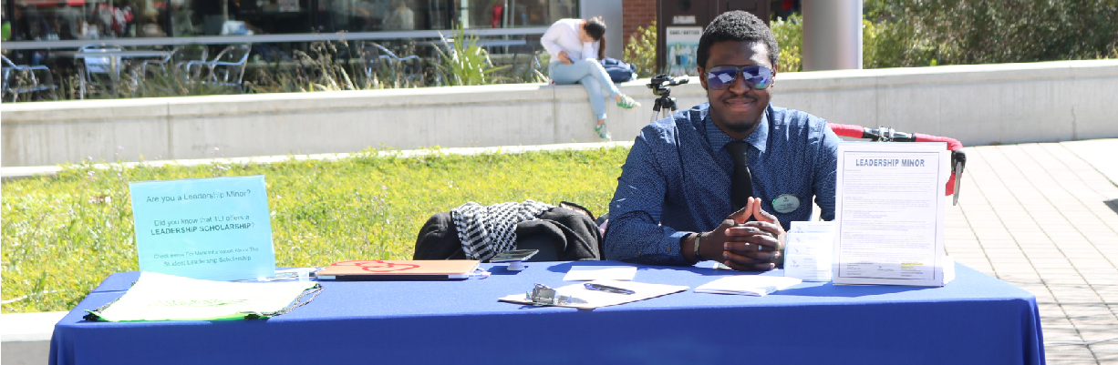 TLI student employee sitting at a table outside at Market Days