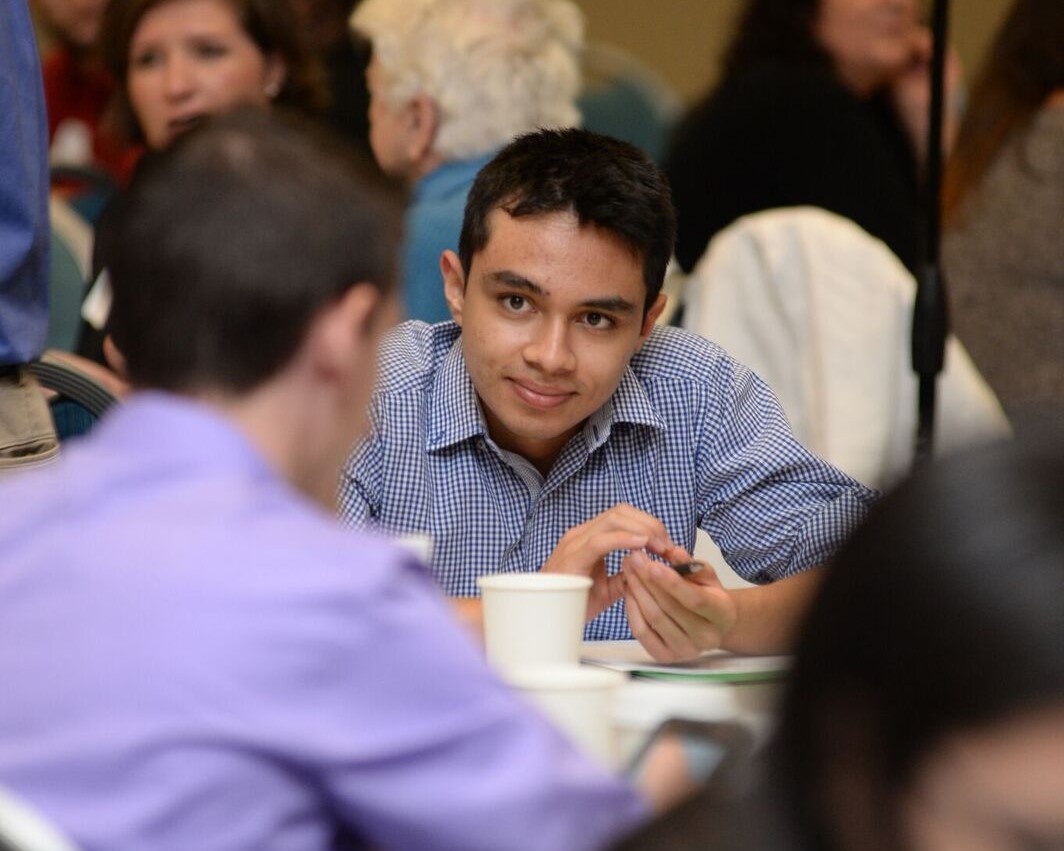 Male student looking ahead and smiling while sitting at a table at the annual Leadership Summit