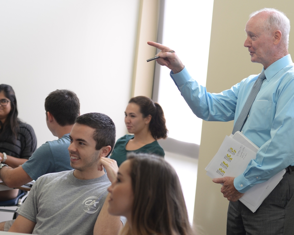Professor Rick Tryon standing in class pointing while teaching with smiling students seated nearby