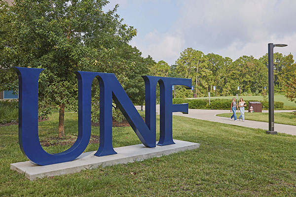 two students walking by a sculpture of the unf letters