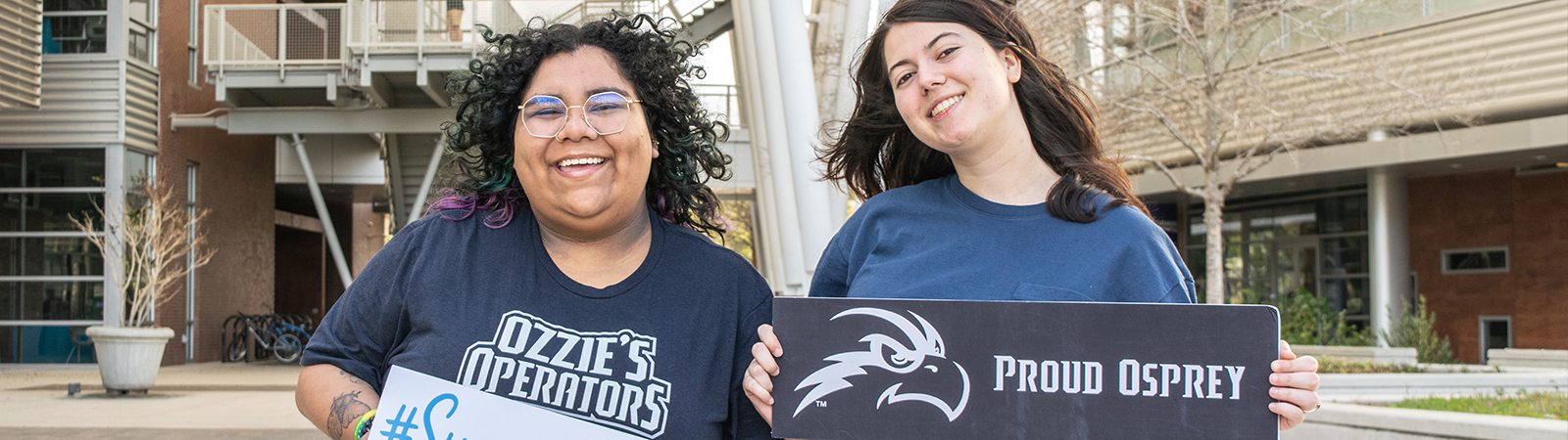 two students smiling holding up signs with proud osprey