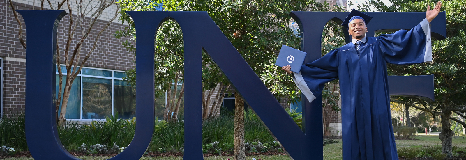 Graduate standing in front of the UNF letters.