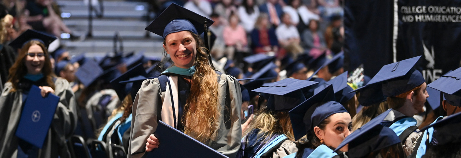 UNF Graduate Student at commencement holding up their recently received diploma