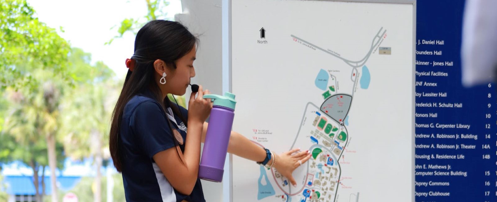 A UNF student tour guide gesturing towards a campus map