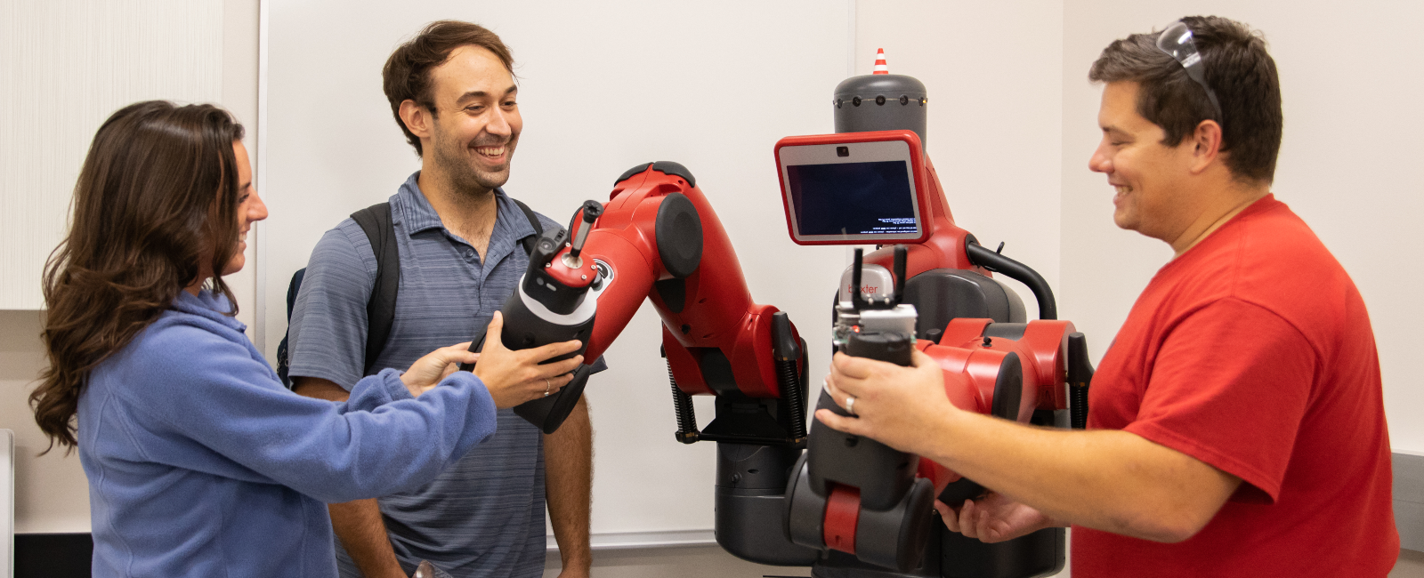 Two males and one female student in an engineering lab with a red machine all smiling