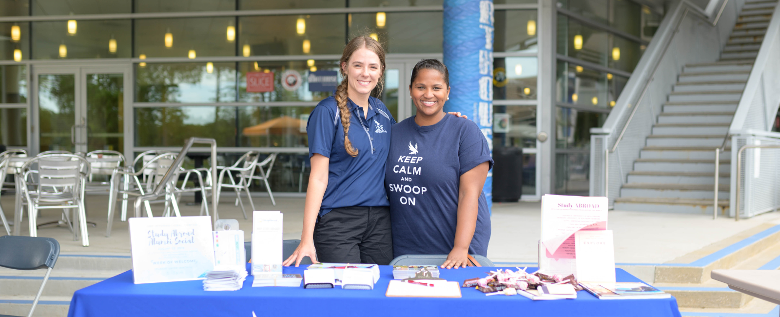 Two female workers in UNF t-shirts standing at an informational table outside smiling