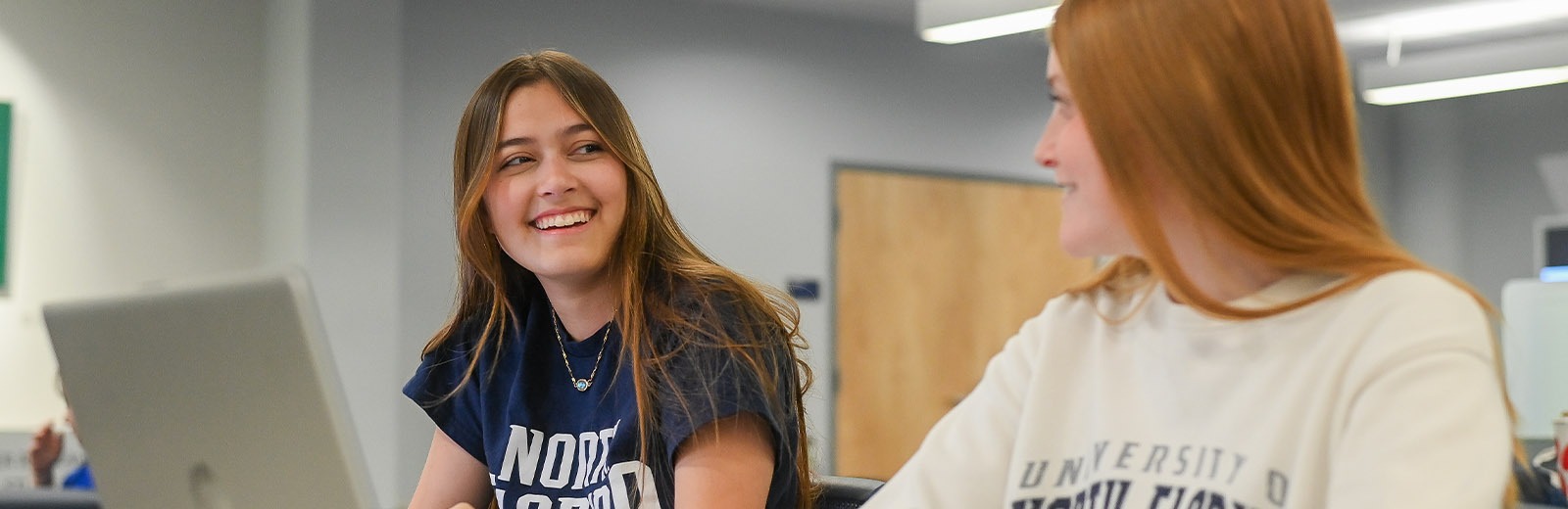 Two students in the UNF library smiling in front of a laptop