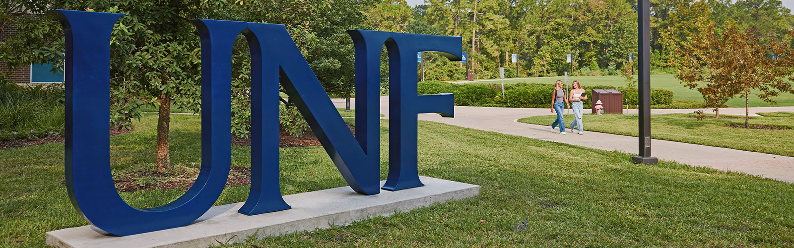 A picture of a UNF sign on campus with two students walking by