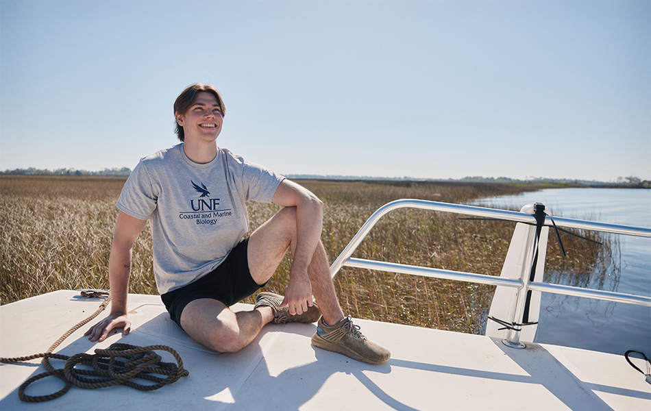 Student in a unf shirt sitting on a boat and smiling