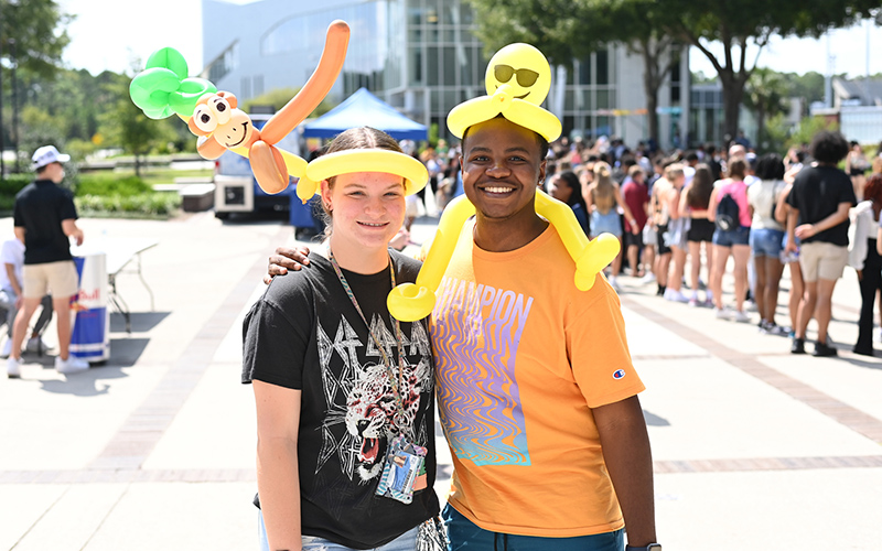 two students with balloon hats on with a crowd behind them